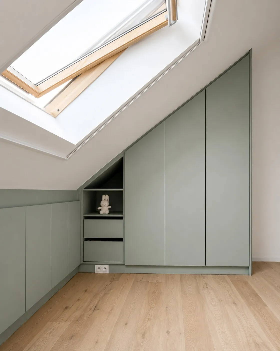 Hoge kast in saliegroen die op verstek meeloopt met de dakhelling, met open legvakken en lades in de lagere hoek